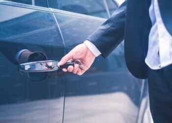 Hand of businessman opening door of car with key.