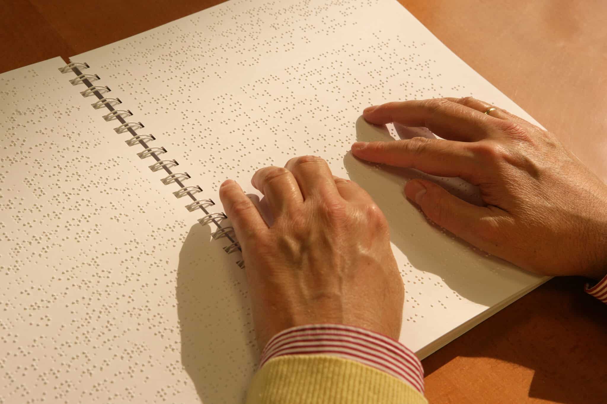El Braille cumple 200 años de evolución: del punzón a la tecnología 1 Las manos de una persona ciega leen un libro en braille scaled El Braille cumple 200 años de evolución: del punzón a la tecnología